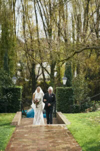 Bride walking with her father on a garden pathway during wedding.