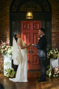 Happy bride and groom holding hands in front of a red door at their wedding.
