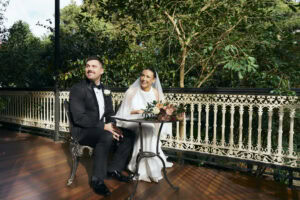 Bride and groom sitting at a table on a decorated outdoor balcony.