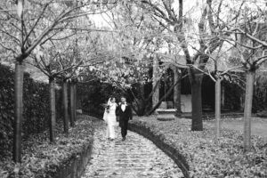 Black and white photo of a bride and groom walking on a garden path.