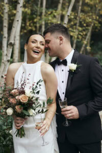 Happy bride and groom celebrating outdoors with champagne and flowers.