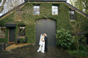 Bride and groom kissing in front of a green ivy-covered barn.