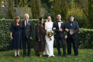 Wedding celebration with six people outdoors in a garden setting.